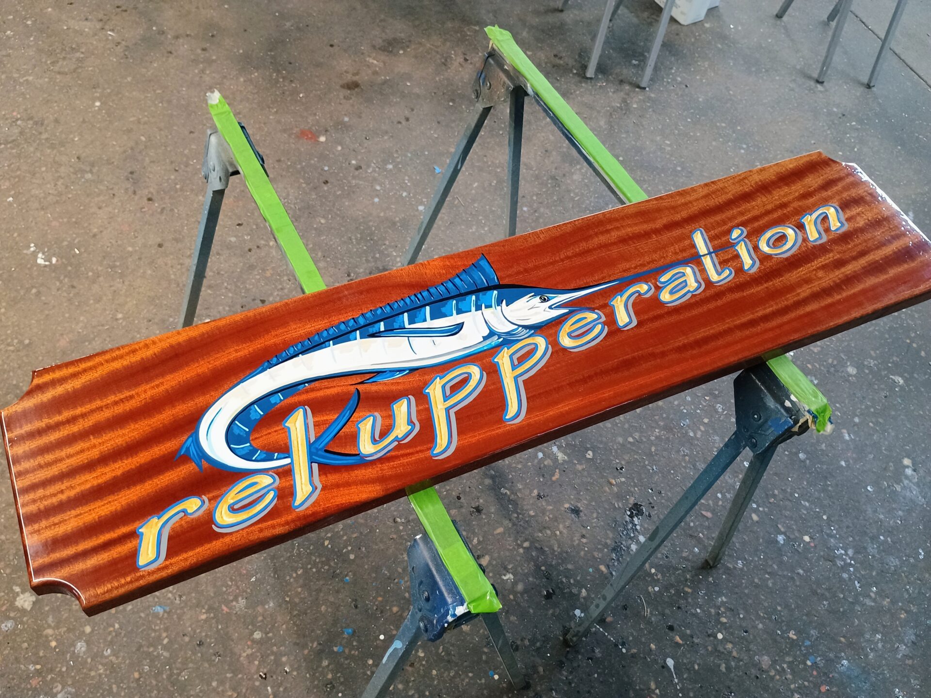 gold leaf letters with blue outline and gray drop shadow on varnished mahogany