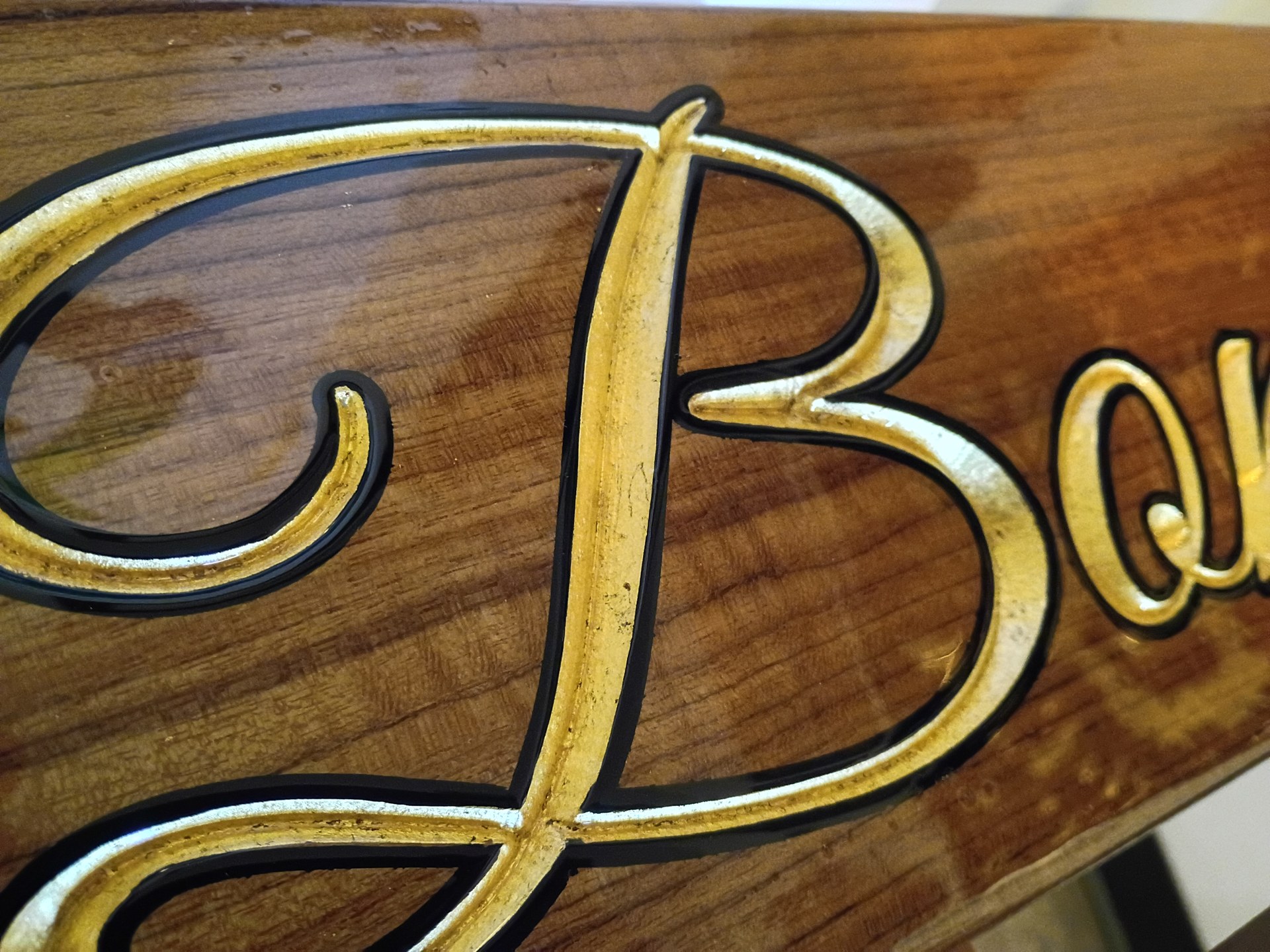 Close-up of the gold leaf script B on the Bonnie Sue carved teak quarterboard with a black outline