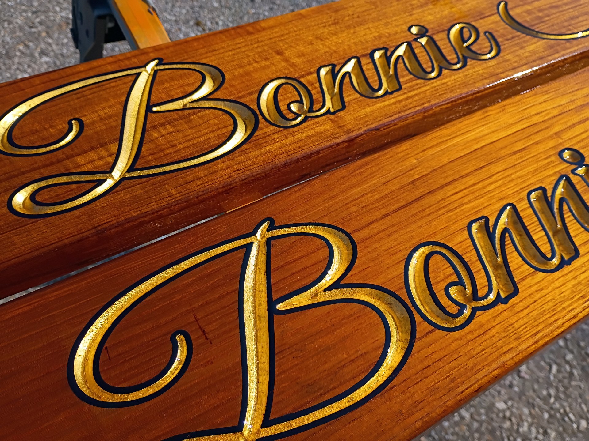 Gold leaf script lettering on the Bonnie Sue teak quarterboards in the sun